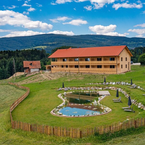 Der Bauernhof mit einem Badeteich und Liegewiese vor der umliegenden Hügellandschaft.