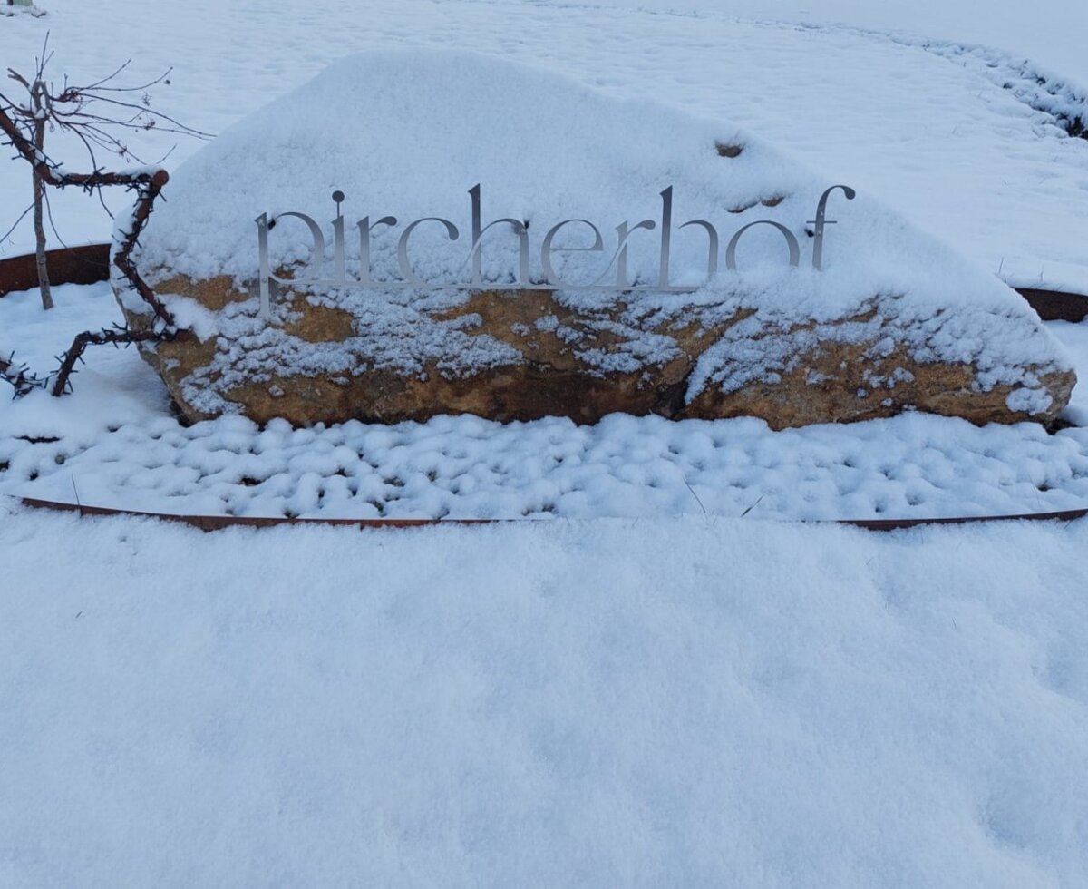 Das verschneite Eingangsschild des Bauernhofs "Pircherhof" mit einem dekorativen Stern.