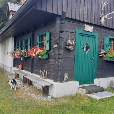 Der Hof mit dunkler Holzfassade, grünen Fensterläden, bunten Blumenkästen und Holzbänken vor dem Eingang.