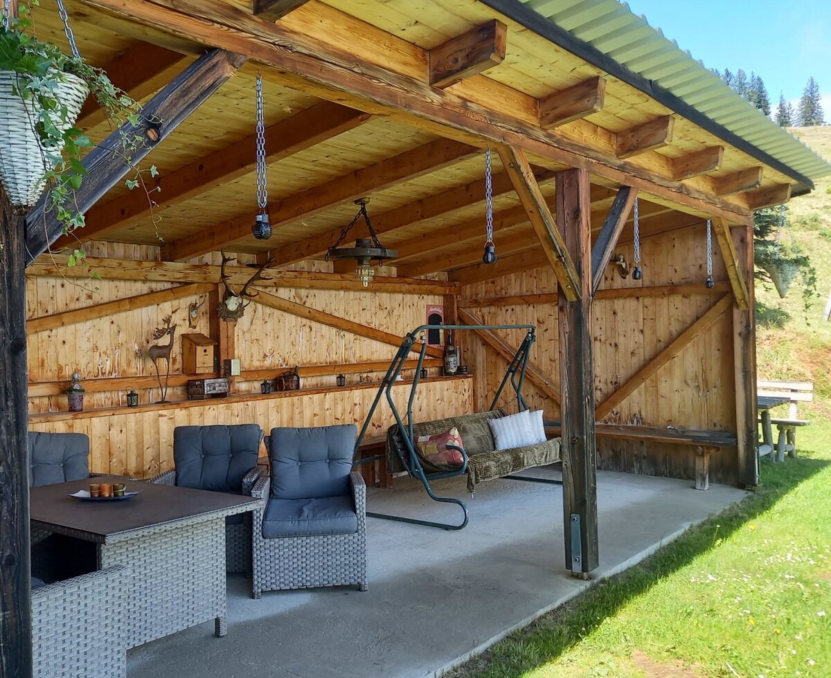 Überdachter Sitzbereich des Hofs mit Korbtisch, Stühlen und Schaukelbank.