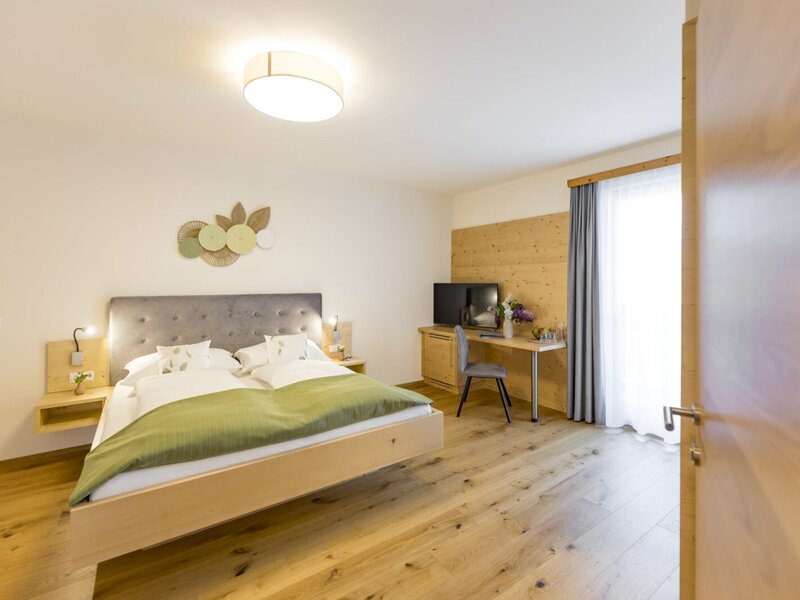 Doppelzimmer mit großem Bett, Holzboden, Schreibtisch, Fernseher und Zugang zum Balkon.