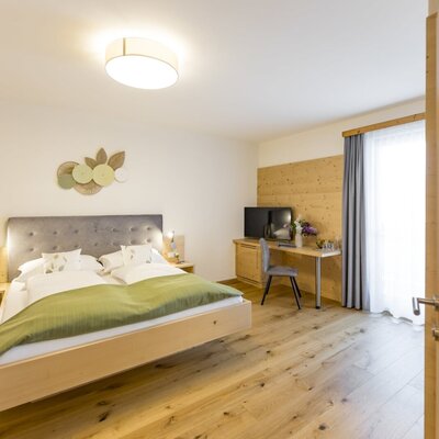 Doppelzimmer mit großem Bett, Holzboden, Schreibtisch, Fernseher und Zugang zum Balkon.