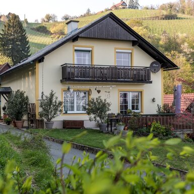 Die Außenansicht des Bauernhofs mit Balkon, Gartenterrasse und den umliegenden Weinbergen.