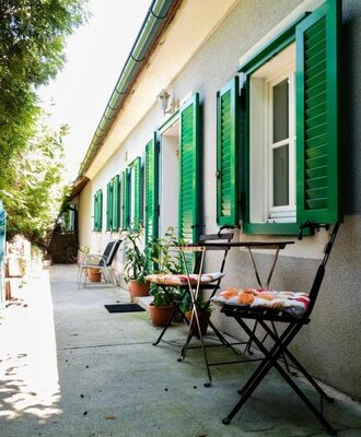 Ein Außenbereich des Bauernhofs mit grünen Fensterläden und einem gepflasterten Sitzplatz mit Tisch und Stühlen.