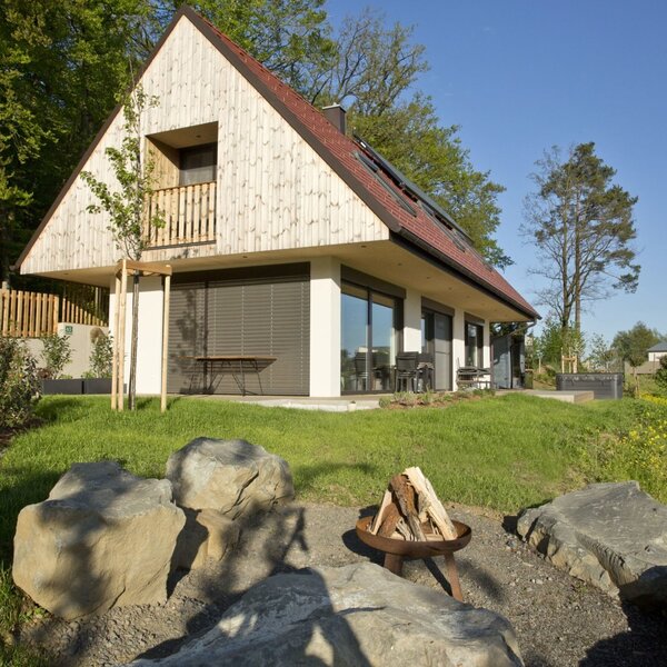 Der Bauernhof mit Holzbalkon im Obergeschoss, Terrassenzugang im Erdgeschoss, Rasenfläche und Feuerstelle.