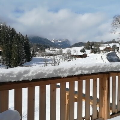 Blick vom Balkon des Bauernhofs auf die verschneite Winterlandschaft mit Bergen und Dorf.
