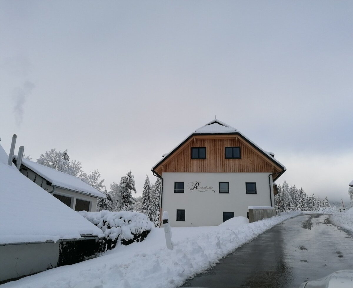 Der Bauernhof im Winter, mit einer modernen Fassade, Holzgiebel und einer geräumten Zufahrtsstraße.