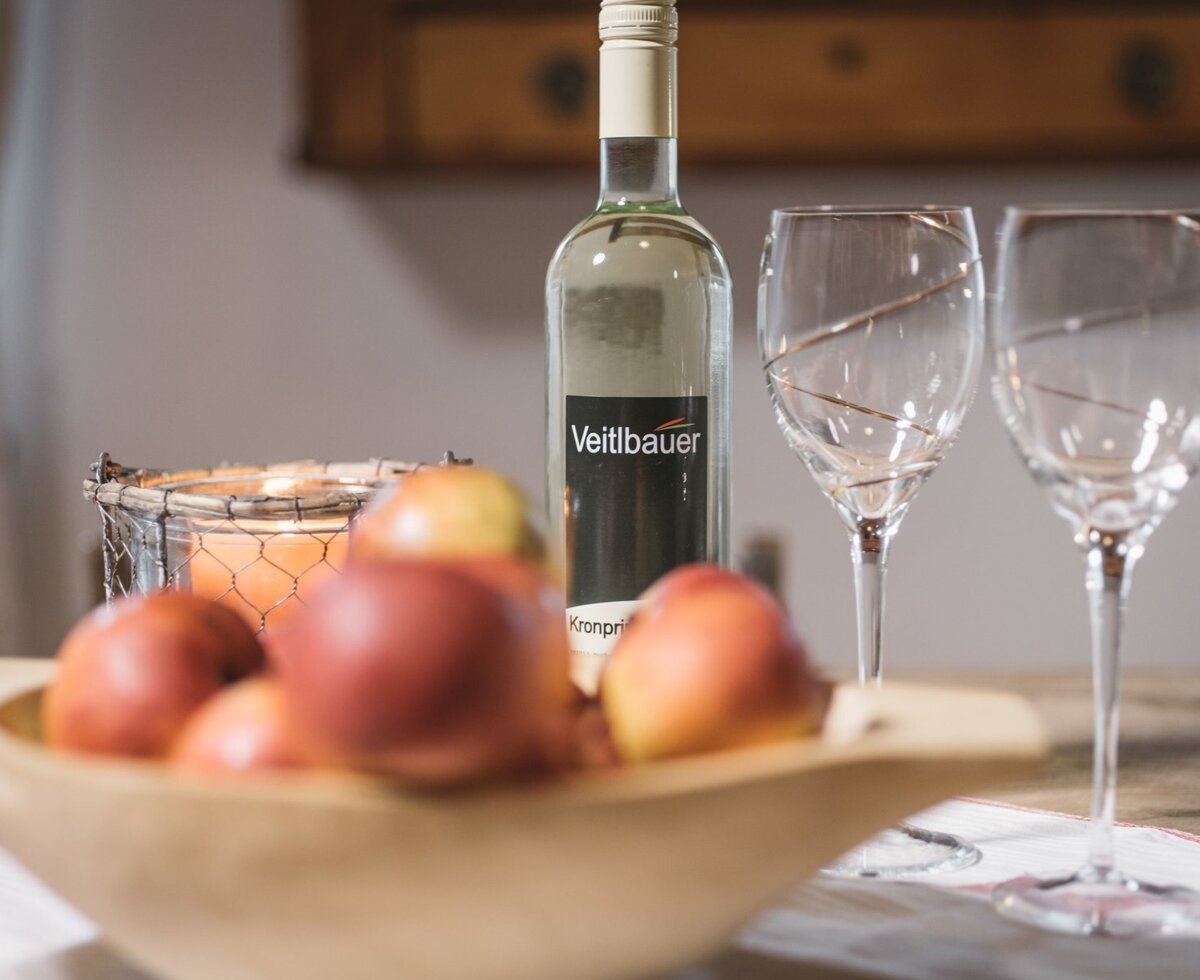 Flasche Wein, zwei Weingläser, eine Schale mit frischem Obst und eine brennende Kerze im Bauernhof.