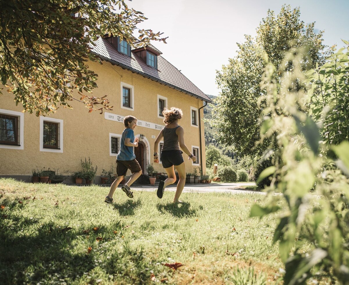 Kinder spielen auf der Rasenfläche vor dem Bauernhof.