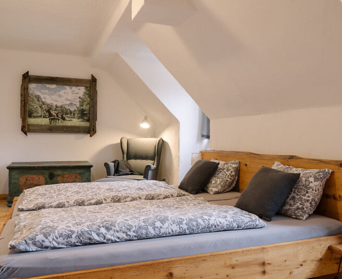 Bacherlrauschn:Schlafzimmer im Bauernhof mit Doppelbett, Dachschräge und Lesesessel.