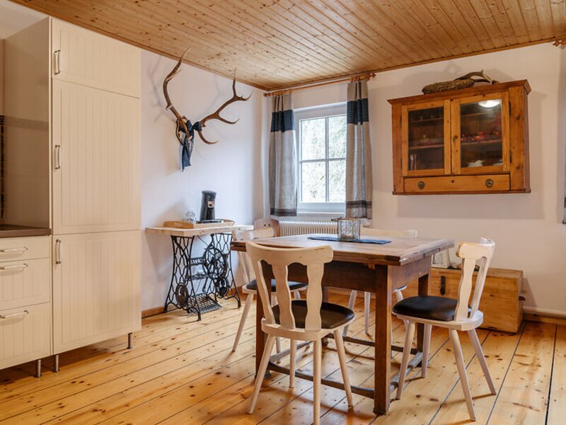 Bacherlrauschn:Essbereich im Bauernhof mit Holztisch für Mahlzeiten, Stühlen und einer teilweise sichtbaren Küchenzeile.