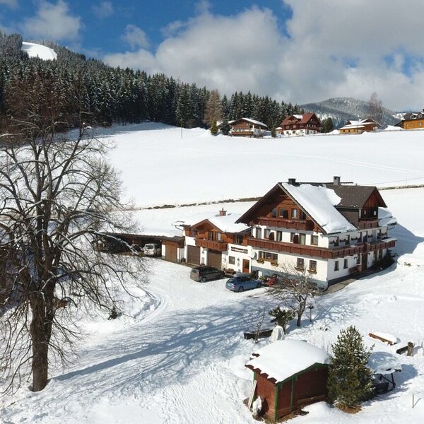 Der Bauernhof in einer verschneiten Winterlandschaft mit umliegenden Bergen.