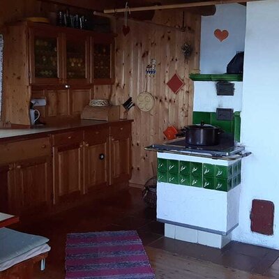 Wohnküche im Hof mit Esstisch, traditionellem Kachelofen und Einzelbett.