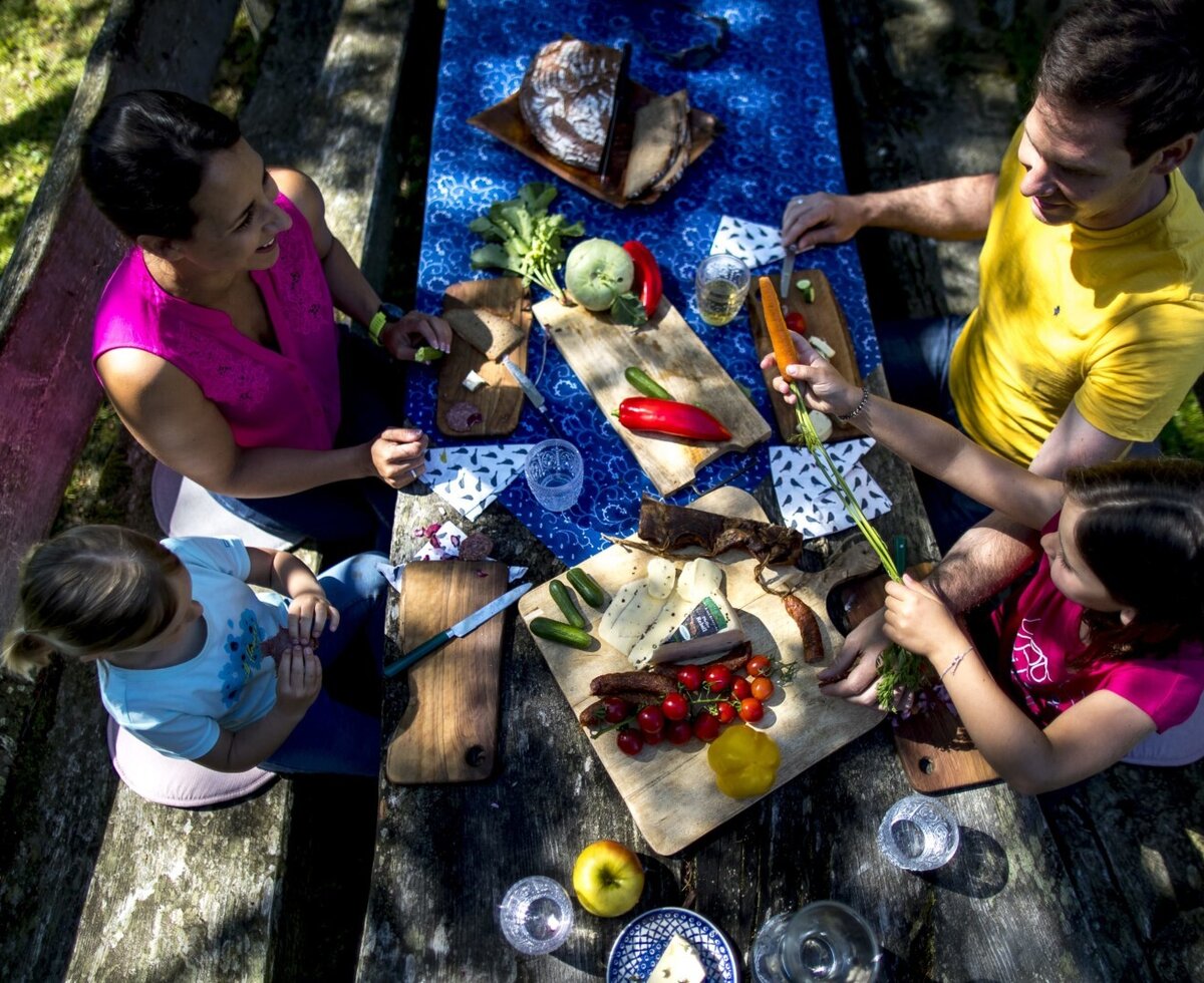 Unsere Gäste lassen sich ihre Jause am großen Holztisch unter freiem Himmel schmecken.