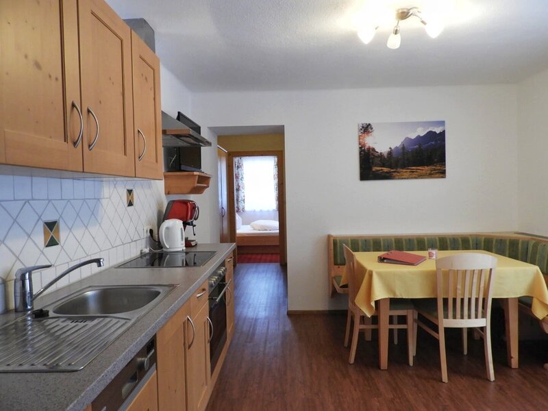 Voll ausgestattete Küche mit Kochfeld, Backofen und Spüle sowie Essbereich mit Eckbank im Appartement auf dem Bauernhof, mit Durchgang zu einem Schlafzimmer.