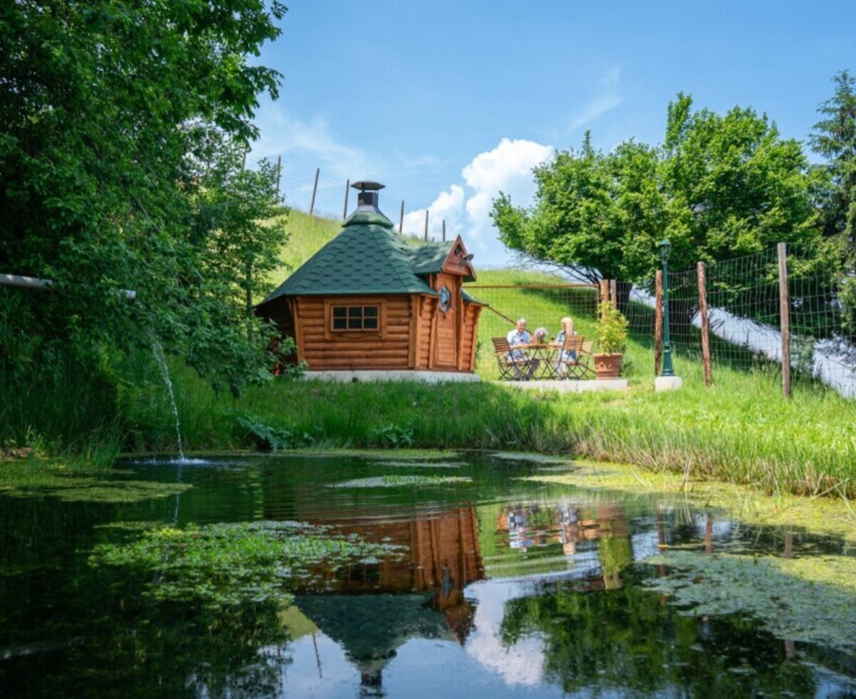 Der idyllische Garten des Ferienhauses mit einer gemütlichen Grillhütte und einem ruhigen Gartenteich.