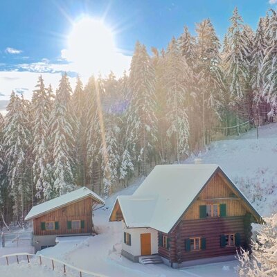 Ein einladendes Ferienhaus inmitten einer tief verschneiten Winterlandschaft, umgeben von sonnenbeschienenen Tannenwäldern.