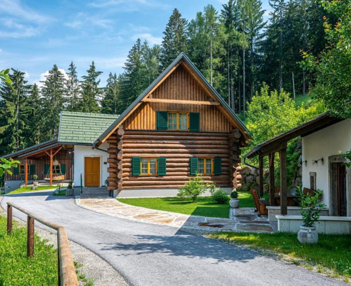 Das Chalet in traditioneller Blockbauweise, umgeben von grünen Wäldern und einer gepflegten Rasenfläche.