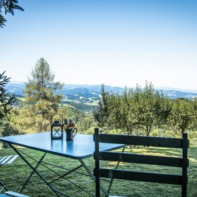 Ein Sitzbereich im Freien auf dem Hof mit Tisch und Stühlen sowie Panoramablick auf die bewaldeten Hügel.