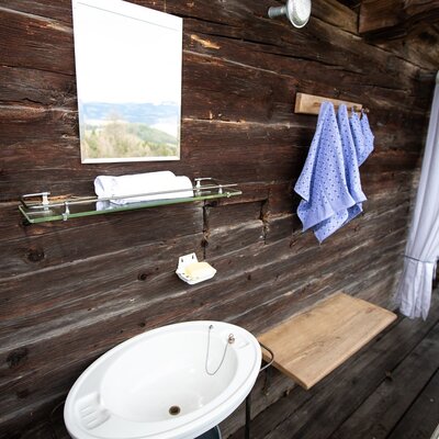 Außenwaschbecken mit Spiegel und Handtüchern an der Holzwand des Hofes.