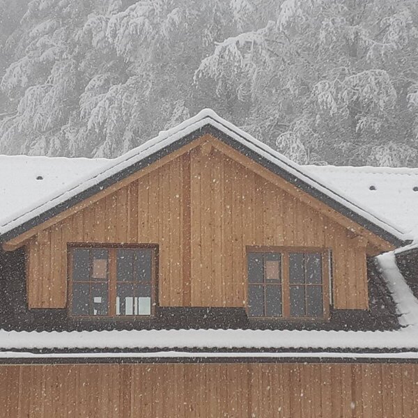 Verschneiter Bauernhof mit Holzfassade und Gaubenfenstern während des Schneefalls.