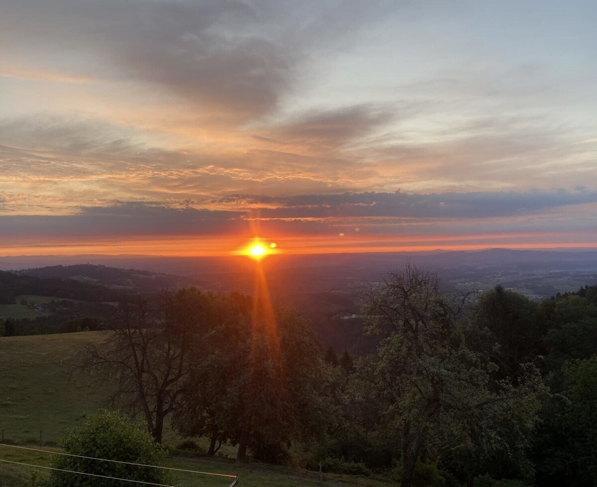 Sonnenaufgang über dem Tal und den umliegenden Hügeln, sichtbar vom Bauernhof.