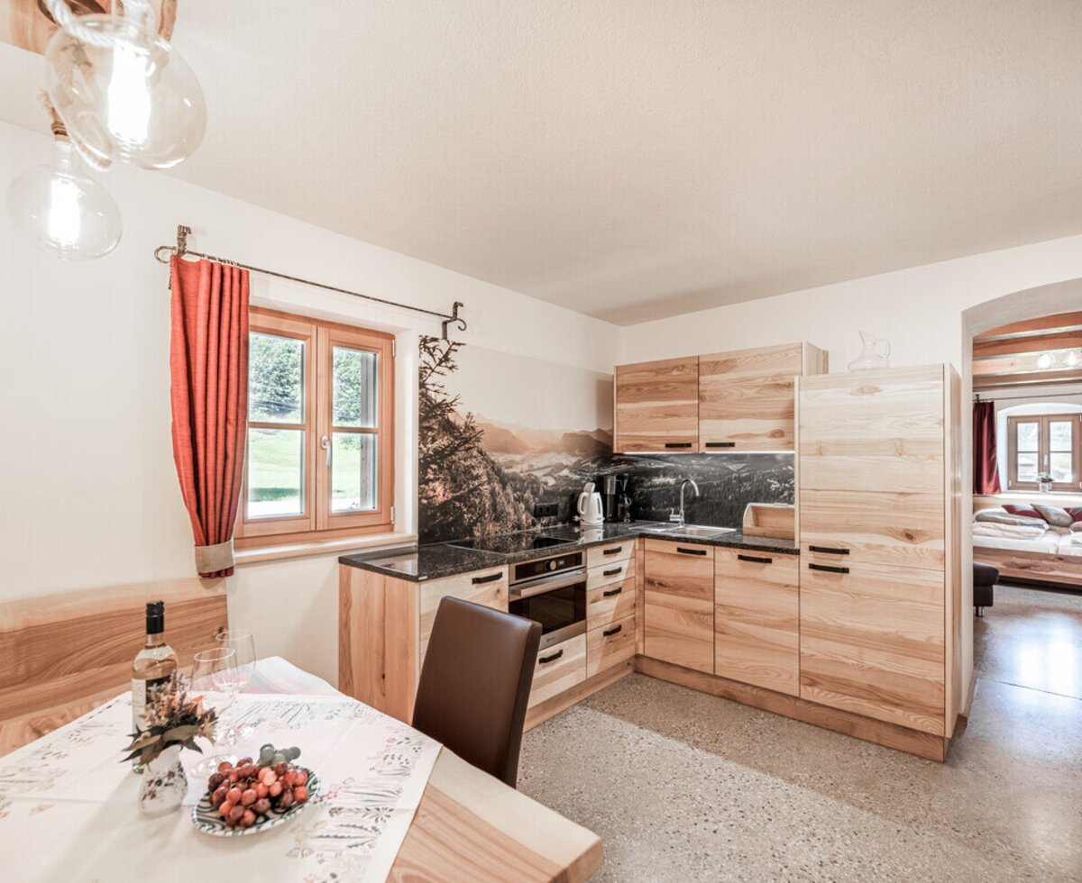Die Ferienwohnung auf dem Bauernhof verfügt über eine Küche mit Vollholzmöbeln, Essbereich und direktem Zugang zu einem Schlafzimmer.