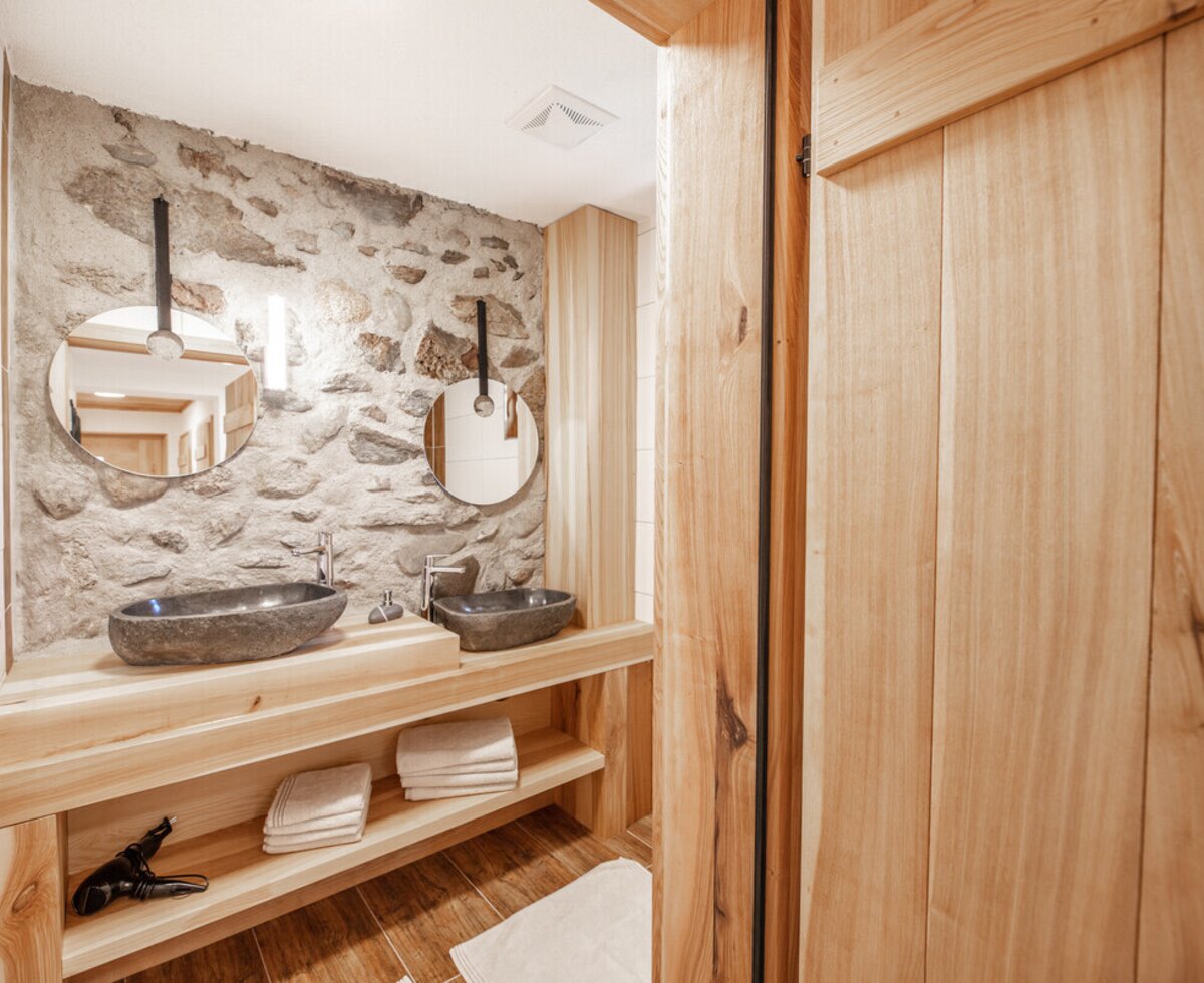 Badezimmer in der Ferienwohnung auf dem Bauernhof mit zwei Steinwaschbecken, Waschtisch aus Vollholz und Natursteinwand.