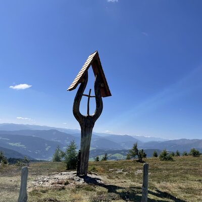 Holz-Marterl auf einer Anhöhe mit Weitblick über die umliegende Berglandschaft.