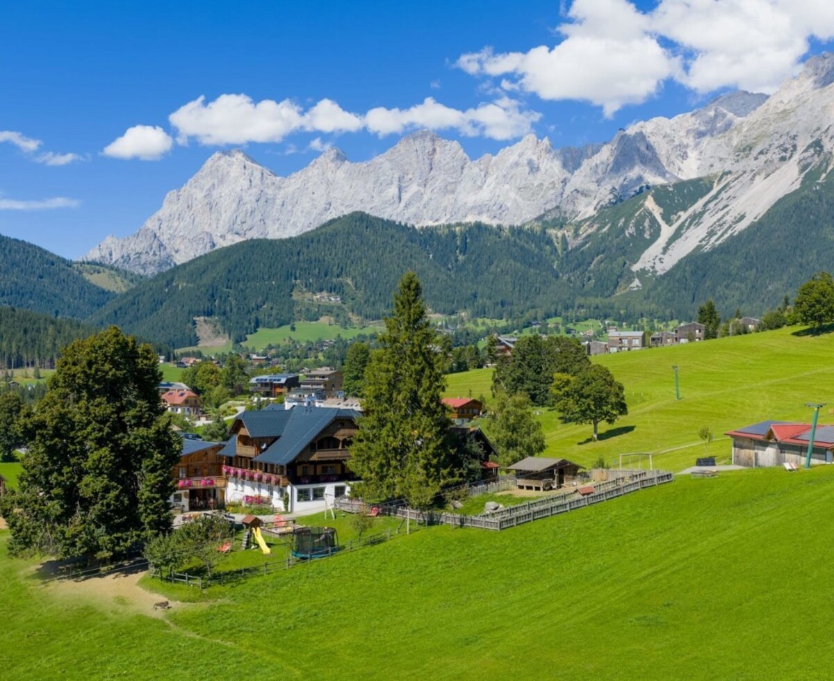 Der Bauernhof mit Blick auf die Bergwelt, umgeben von grünen Wiesen.