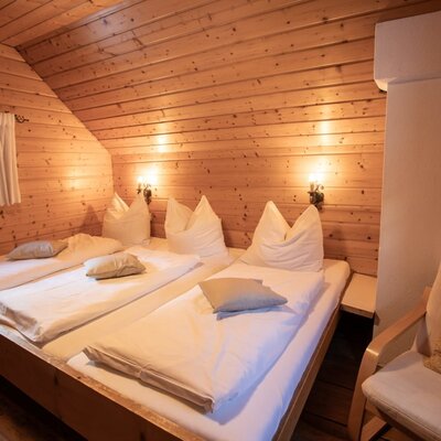Schlafzimmer im OG mit Familienbett, Holzwänden, einem kleinen Fenster und einem Sessel.