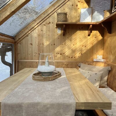 Der Wintergarten des Ap­par­te­ments mit Esstisch, Sitzbank.