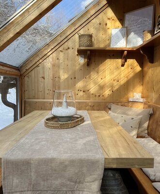 Der Wintergarten des Ap­par­te­ments mit Esstisch, Sitzbank.