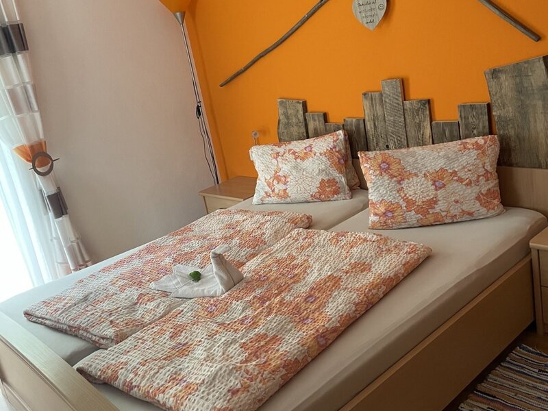 Doppelzimmer im Bauernhof mit Holz-Kopfteil und einer orangefarbenen Wand, dekoriert mit Rechen.