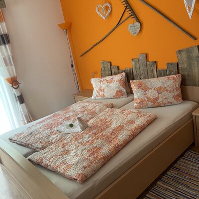 Doppelzimmer im Bauernhof mit Holz-Kopfteil und einer orangefarbenen Wand, dekoriert mit Rechen.