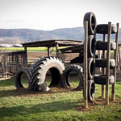 Kinderspielplatz mit Reifen auf der Wiese des Bauernhofs, umgeben von Feldern und Hügeln.