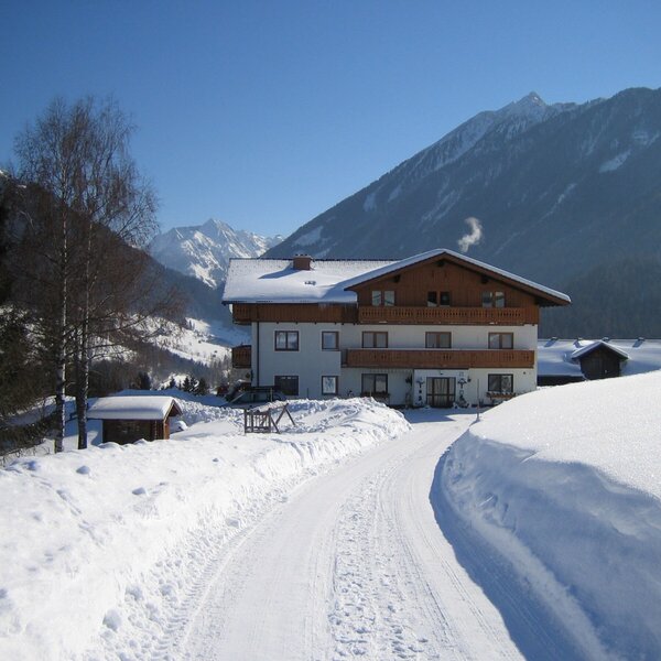 Die winterliche Außenansicht des Bauernhofs mit Balkonen, verschneiter Zufahrt und Bergblick.