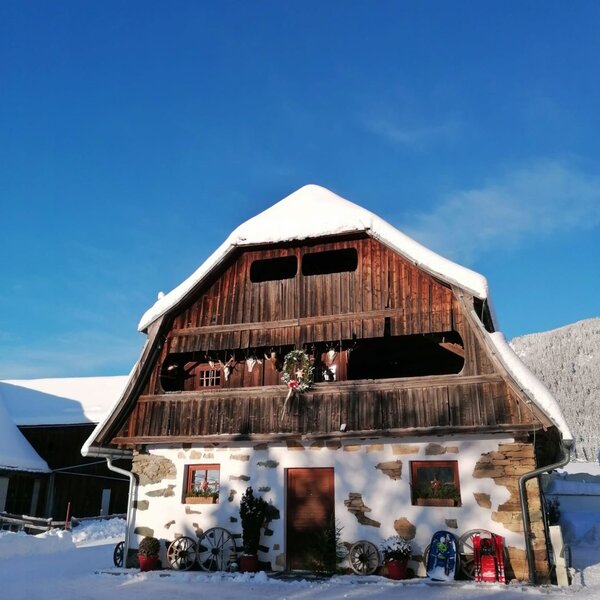 Außenansicht des Bauernhofs mit schneebedecktem Dach und rustikaler Fassade im Winter.
