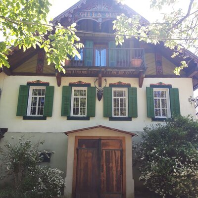 Die Außenansicht des Hofes mit grünen Fensterläden, einem Balkon, der Aufschrift "VILLA LUI" am Giebel und einem Hirschgeweih als Dekoration.