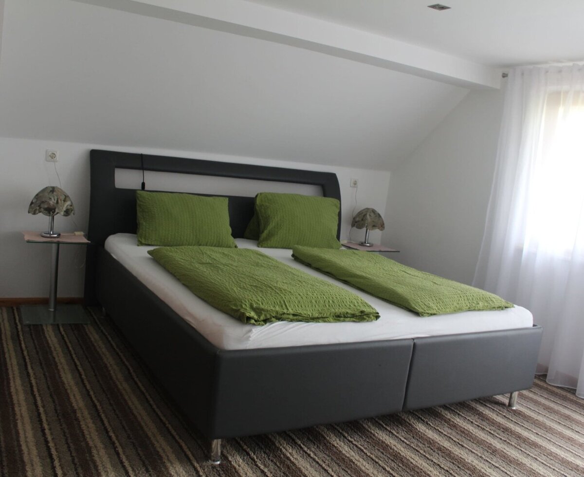 Doppelzimmer mit Doppelbett, grüner Bettwäsche, zwei Nachttischen, Lampen und einem Fenster in der Dachschräge.