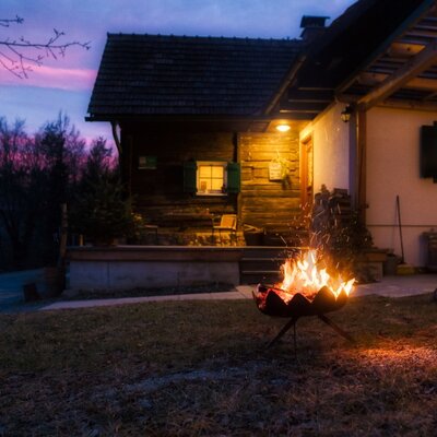 Der Hof mit beleuchteter Fassade, Feuerstelle im Garten und überdachter Pergola am Abend.