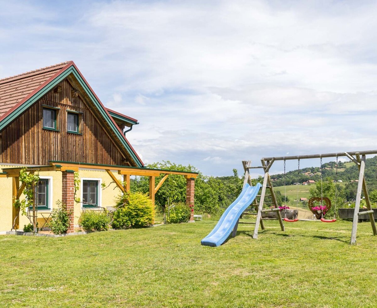 Der Außenbereich des Bauernhofs mit Rasenfläche und einem Kinderspielplatz inklusive Rutsche und Schaukeln. (c) Elisabeth Fröhlich Photography