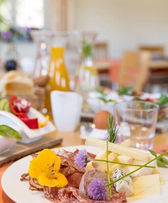 Frühstück auf dem Bauernhof mit einer Platte mit Wurst, verschiedenen Käsesorten, Pastete und essbaren Blüten. (c) Elisabeth Fröhlich Photography