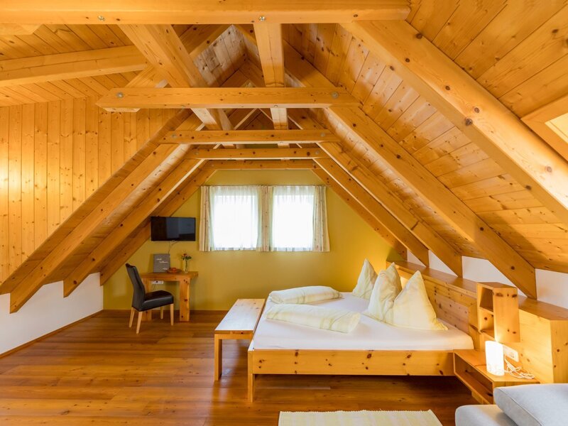 Geräumiges Doppelzimmer im Dachgeschoss des Bauernhofs mit Holzbalken, Holzboden, Doppelbett, Schreibtisch und TV. (c) Elisabeth Fröhlich Photography