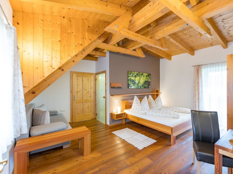 Doppelzimmer im Bauernhof mit Holzbalkendecke, Doppelbett, Sofa und Essbereich. (c) Elisabeth Fröhlich Photography