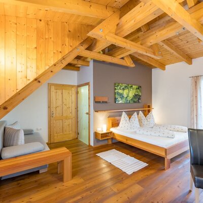 Doppelzimmer im Bauernhof mit Holzbalkendecke, Doppelbett, Sofa und Essbereich. (c) Elisabeth Fröhlich Photography