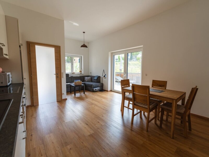 Offener Wohnbereich mit Küchenzeile, Esstisch für vier Personen, Wohnbereich mit Sofa und Zugang zur Terrasse.