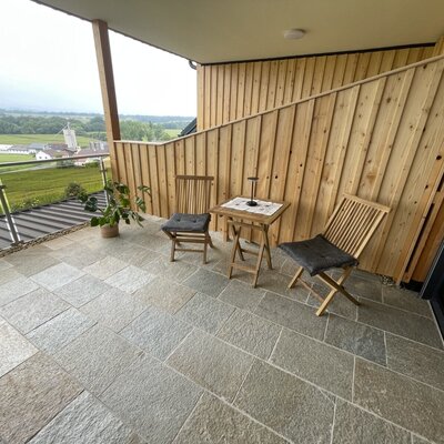 Der Balkon am Hof bietet Steinplatten, Holzmöbel und einen weiten Blick über die Landschaft.