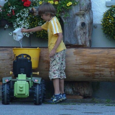 Spielmöglichkeiten für Kinder auf dem Bauernhof mit einem Trettraktor und Wasserspielen.