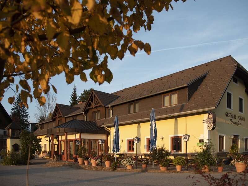 Die Außenansicht des Gasthauses der Frühstückspension auf dem Bauernhof mit Terrasse und Sonnenschirmen.